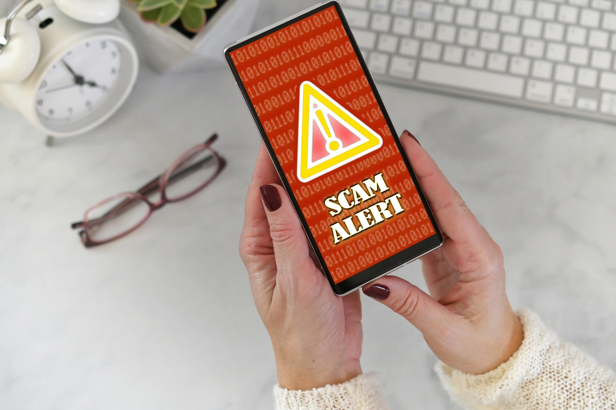 Watch Out for These 4 Common Scams: How to Stay Ahead of Scammers 5 Female holding a phone at desk with Scam Alert warning screen in red and yellow